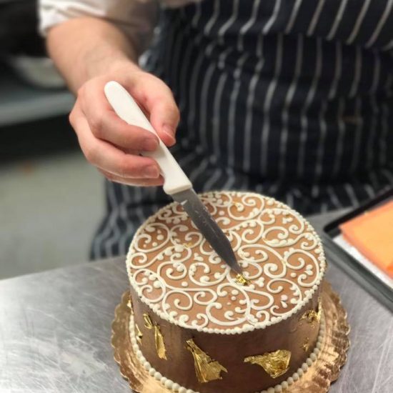 Cutting into a Chocolate Cake with White Frosting and Gold Flakes